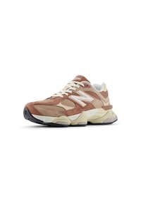 Zapatillas de ante marrón y malla con cordones blancos, una suela gruesa color crema y un logo "N" prominente en el lateral. Presenta un diseño de punta redondeada.