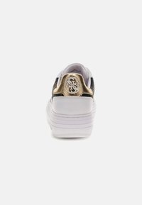 Sneaker bianco con parte superiore nera testurizzata, dettaglio dorato sul tallone e logo. Suola spessa e design della parte posteriore arrotondato.