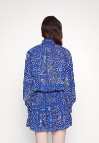 Vestido azul con un estampado de paisley, mangas largas, cintura fruncida y un dobladillo con volantes. Confeccionado con una tela ligera y con cuello fruncido.
