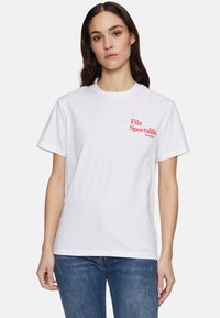 Valkoinen lyhythihainen t-paita, jossa on pyöreä pääntie ja punainen "Fila Sportslife" -logo vasemmassa rinnassa. Valmistettu puuvillakankaasta.