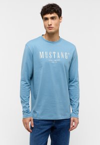 Light blue long-sleeve t-shirt with a round neckline, featuring "MUSTANG JEANS COMPANY" in white lettering across the chest.