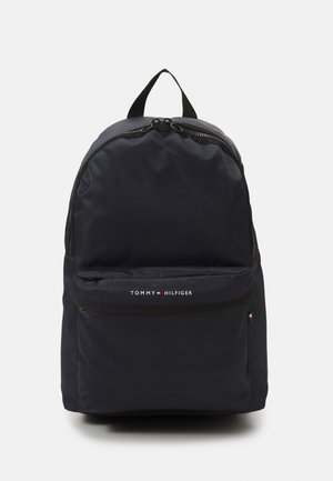 Musta Tommy Hilfiger -reppu, jossa on etutasku vetoketjulla ja kaksi ylävetoketjua, valkoista taustaa vasten.