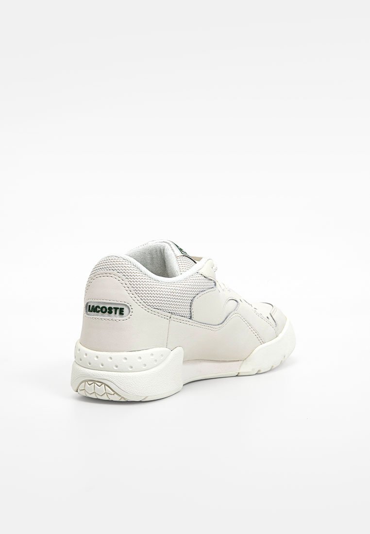 Sneaker blanche en cuir et en maille, avec un dos texturé, un col rembourré et un accent du logo Lacoste vert. Semelle en caoutchouc arrondie.