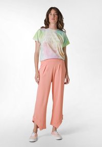 Leichte Batik-T-Shirt in pastellen Farben mit kurzen Ärmeln und weißem Text, kombiniert mit fließenden, korallenfarbenen weit geschnittenen Hosen mit Schlitzsäumen.