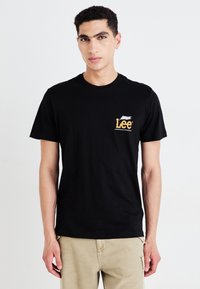 T-shirt en coton noir avec un logo sur la poitrine en jaune et blanc, manches courtes et design classique à col rond.