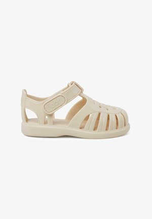 Beige plastic sandal with a strap and cut-out design, featuring an open toe and zigzag pattern across the front. Rubber sole for traction.