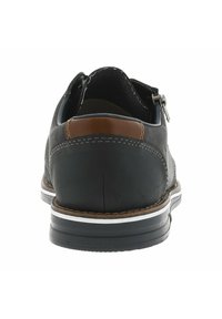 Zapato de cuero negro con un acento en color tostado, costuras blancas y suela de goma. Presenta una abertura con cremallera y un diseño de tacón redondeado.