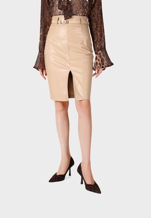Donna che indossa una gonna a matita in pelle beige con spacco frontale e cintura, abbinata a una camicetta marrone trasparente con stampa leopardata e tacchi alti neri.