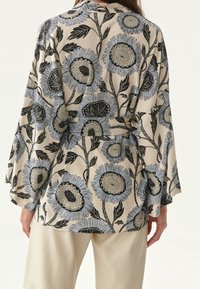 Kimono floreale con girasoli oversize in blu e nero su uno sfondo beige. Presenta maniche larghe e una vita con cintura per una vestibilità regolabile.