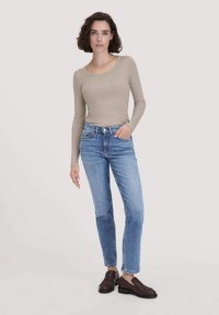 Beige langemouwen top gecombineerd met lichtblauwe rechte spijkerbroek, met voorzakken en bruine instapper met franjes.