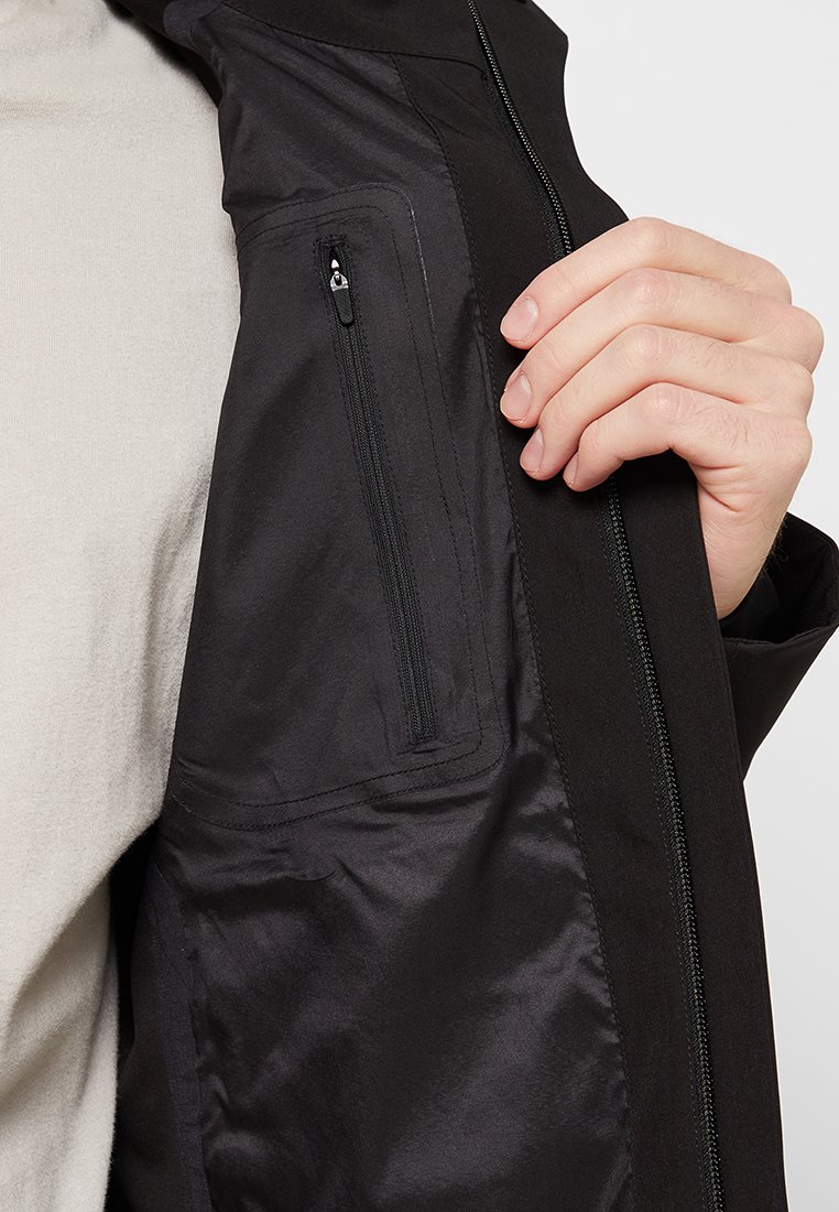 Giacca nera con tasca con zip sulla manica. Il materiale è liscio, con un rivestimento interno a contrasto. Elementi di design minimalisti.