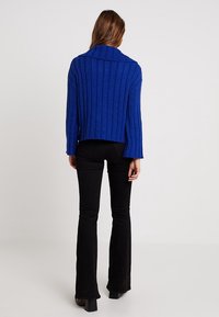 Kongligt blått ribbat tröja med en bred krage och kort design, i kombination med svarta utsvängda byxor. Tyget verkar texturerat och mysigt.