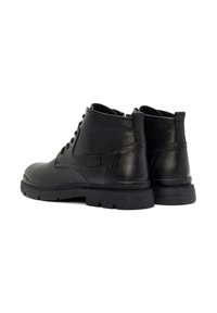 Botas de tobillo de cuero negro con acabado texturizado, que cuentan con un diseño de cordones y suelas de goma gruesas. Se aprecian sutiles acentos laterales.