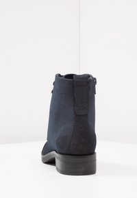 Mörkblå mocka ankelsko med en slät yta, en svart gummisula och en bakre flik för enkel påtagning. Minimalistisk design utan synliga beslag.