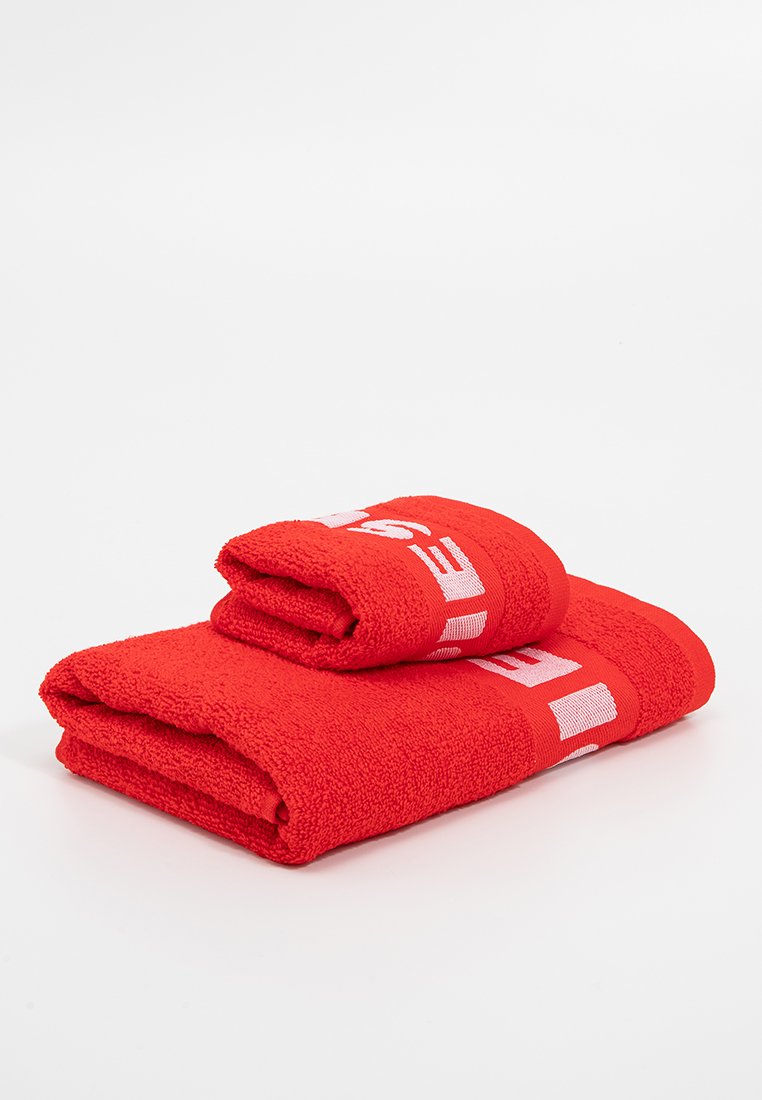 Juego de toallas rojas, con una textura suave y un gran nombre de marca en blanco destacado. Incluye una toalla grande y una más pequeña apiladas.
