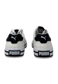 Sneakers bianchi con tomaia in pelle liscia, accenti neri sul tallone e suola in gomma a strisce bianche e nere. Presenta un logo Puma sul retro.