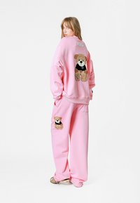 Conjunto de sudadera y pantalones de chándal rosa con aplicaciones de ositos de peluche en la parte trasera y lateral. Tejido suave con corte holgado y hombros caídos.