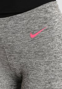 Leggings sportivi grigi con finitura testurizzata, caratterizzati da un logo Nike rosa sulla vita. Il tessuto appare elastico e traspirante.