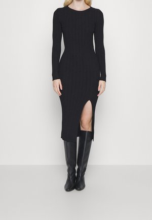 Abito a maglia nera a coste con maniche lunghe, di lunghezza media, con uno spacco alto fino coscia, abbinato a stivali in pelle nera alti fino al ginocchio.
