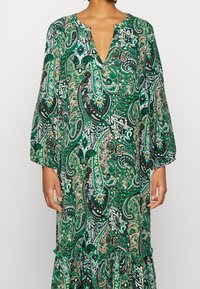 Dlouhá zelená šaty s paisley vzorem, V-výstřihem, 3/4 rukávy s volány a patrovým lemem. Vyrobeno z lehkého materiálu.