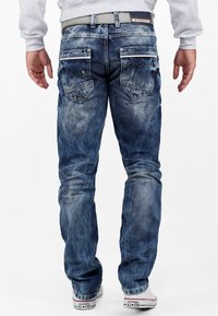 Faded blue denim jeans with five pockets, visible stitching, and a gray belt. Worn with white Converse shoes featuring a logo on the side.