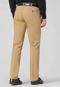 Khaki chino's met een rechte pijp, van een katoenmix, twee achterzakken en een zwarte riem. Gecombineerd met zwarte sneakers met rode accenten.