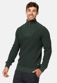 Suéter de punto verde oscuro con un cuello alto y media cremallera. Puños y dobladillo acanalados, con un panel frontal texturizado y un sutil detalle de logotipo.
