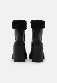 Schwarze Leder-Stiefeletten mit einem flauschigen schwarzen Lammfellbund, dickem hohen Absatz und strukturierten Oberflächen. Ideal für den Winter.