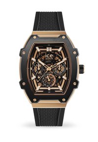Montre noire et dorée avec boîtier octagonal, bracelet en caoutchouc noir, cadran complexe, présentant des index horaires et trois sous-cadrans. Détail texturé du bracelet.