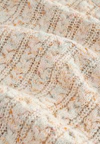 Un tissu tricoté couleur crème avec un motif en zigzag texturé et de petites accents en fil dans des tons pastel de rose, d'orange et de gris.