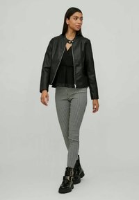 Veste en cuir noir avec un col rond, associée à un haut noir et un pantalon à motif pied-de-poule. Bottes noires élégantes à talons avec des boucles.