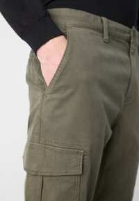 Pantalones cargo verde oliva hechos de tejido suave, con bolsillos laterales, un corte relajado y detalles de costura visibles.