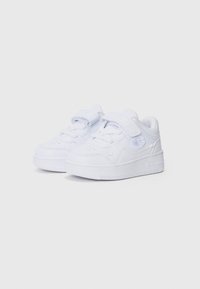Chaussures de sport blanches en cuir synthétique, avec un bout rond, une sangle à crochets et une semelle en caoutchouc texturée. Logo affiché sur le côté.