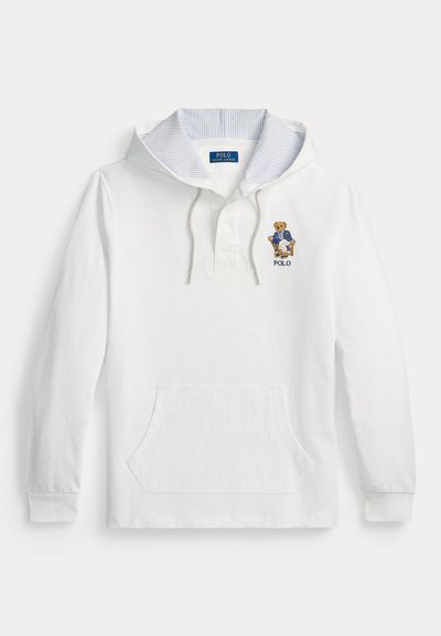 Sweat à capuche blanc avec capuche intérieure rayée, poche avant et ours brodé portant un blazer bleu assis sur une chaise, avec le texte "POLO" en dessous.