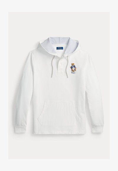 Sweat à capuche blanc avec capuche intérieure rayée, poche avant et ours brodé portant un blazer bleu assis sur une chaise, avec le texte "POLO" en dessous.