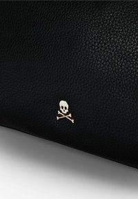 Sort tekstureret læderpung med et metallisk gyldent dødningehoved- og korsknoglesymbol. Glat overflade og detaljeret kornmønster.