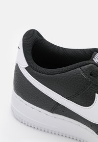 Črne usnjene superge z teksturirano površino, belim ukrivljenim logotipom, mrežastim ovratnikom in belim gumijastim podplatom.