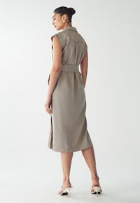 Ärmelloses, knielanges Kleid in hellem Taupe mit vertikalen Nadelstreifen. Es verfügt über einen kragenlosen Ausschnitt, eine taillierte Taille und einen seitlichen Schlitz.