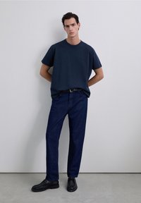 Marineblauw T-shirt met korte mouwen, gecombineerd met donker denim broek en zwarte schoenen. Eenvoudig ontwerp en relaxte pasvorm, minimale versieringen.