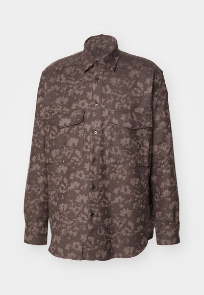 Camisa de manga larga hecha de un tejido marrón texturizado con un patrón de hojas, que cuenta con dos bolsillos en el pecho y cierre frontal con botones.