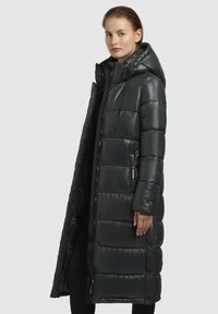 Dlhý čierny puff coat, lesklý materiál, s kapucňou, so zipsom a patentkami, priliehavý dizajn s vypchávkovanými časťami, dosahuje po polovicu lýtok.