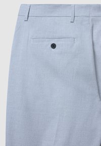 Pantaloni a trama grigia chiara con una finitura texturizzata, caratterizzati da una tasca posteriore con un bottone nero e passanti per la cintura in vita.