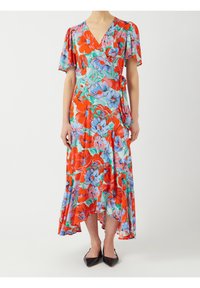 Robe portefeuille florale avec des fleurs rouges, bleues et roses, manches courtes à volants, décolleté en V, et ourlet asymétrique, associée à des ballerines noires à bout pointu.