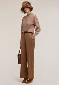 Neulottu vaaleanpunainen villapaita, korkeakauluksinen, yhdistetty korkeavyötäröisiin, leveälahkeisiin ruskeisiin housuihin. Asusteina leopardikuvioinen bucket-hattu ja ruskea laukku.