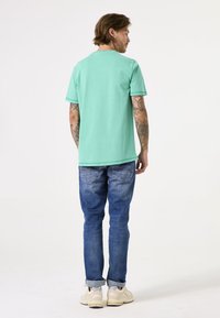 Mintgroene t-shirt met korte mouwen, gecombineerd met blauwe denim jeans. Het shirt heeft een eenvoudige ronde halslijn en een casual pasvorm. Witte sneakers maken de outfit compleet.