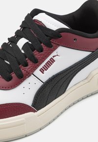 Sneakers Puma con pelle nera e bordeaux testurizzata, dettagli bianchi. Lacci neri, suola in gomma crema e dettaglio del logo presente.