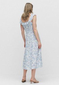 Kwiatowa sukienka midi w kolorze białym z niebieskim wzorem, z falbaniastymi ramiączkami i dopasowanym gorsetem. Gładki materiał z rozszerzanym dołem.