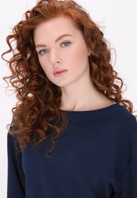 Maglietta a maniche lunghe di colore navy con scollatura ampia. Tessuto morbido e vestibilità comoda. La modella ha lunghi capelli rossi e ricci, con un trucco naturale.