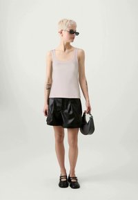 Lys rosa tettsittende tanktop med firkantet utringning, kombinert med svarte oversized shorts i imitert skinn og en liten svart håndveske.