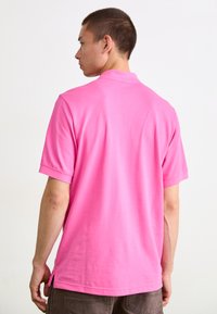 Kortærmet polo skjorte i lys pink bomuld med klassisk krave, sideslids og en glat tekstur. Bagansigt vist.